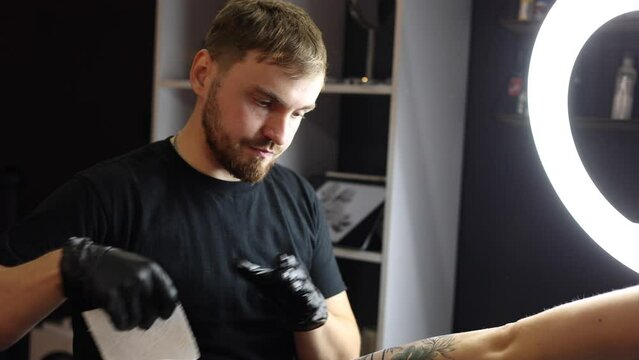 Tattoo artist moisturizes the hand by spaying it with water from a spray bottle