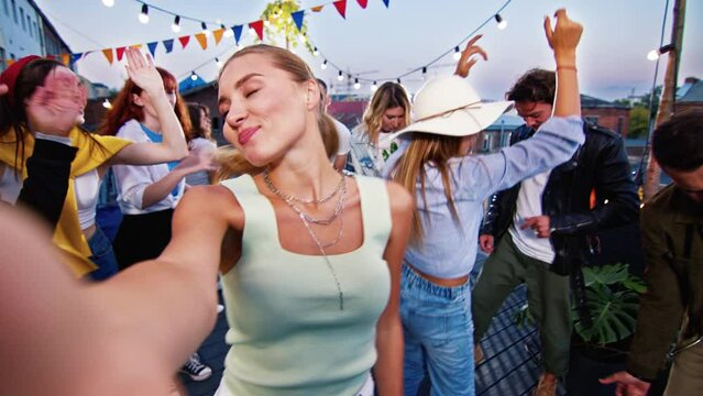 POV of beautiful young female blogger recording selfie video showing music event on top of roof. Attractive happy people dancing having fun listening to music of band playing on guitar and drums.