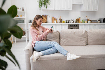 young woman messaging on smartphone while resting on couch.