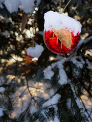 red ball on a Christmas tree covered with snow. the toys on the Christmas tree are covered with snow. winter holiday decorations on the Christmas tree. red ball with orange pattern covered with snow.