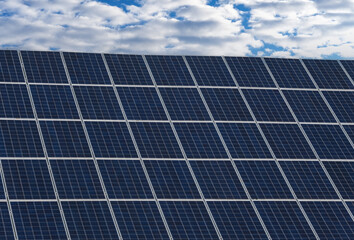 Blick auf eine große Photovoltaikanlage zusammengesetzt aus mehreren Solarpanels vor blauem und bewölktem Himmel - obrazy, fototapety, plakaty