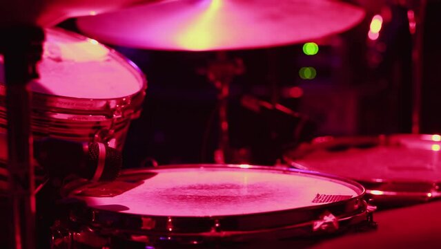 a close-up of a musician actively playing drums and hi-hat, illuminated by pink-red light. The concept of a rehearsal, a concert