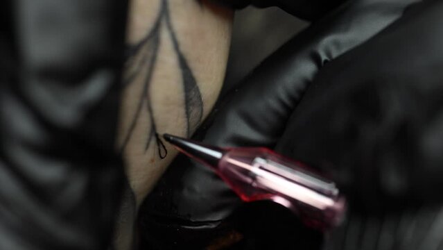 Macro video of a young professional tattoo master introduces black ink into the skin using a needle from a tattoo machine. Tattoo on hand close-up