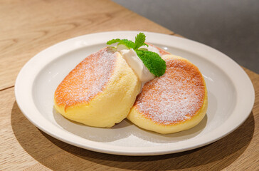 Japanese style sluffy souffle pancake dessert with cream served on a white plate on a wooden table