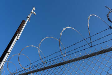 Fence with razor wire with blue sky in background. 
Razor wire is made up of high tensile core wire...