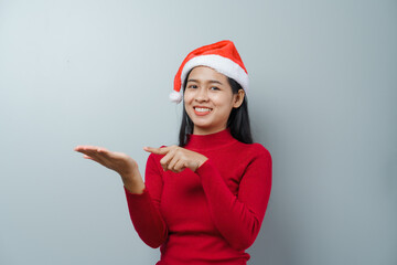 Pretty lovely lady asian thai women in red sweater and santa christmas hat isolated over grey background. hands pointing