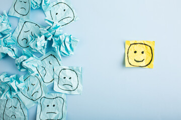 A sad face watching smiling faces from afar. Happy and sad faces drawn on blue stickers. Concepts...