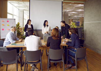 Fototapeta na wymiar Diverse businesspeople gather at desk at team meeting in office brainstorm and collaborate. Employees talk in group discuss business ideas and project strategy. Cooperation and teamwork concept.