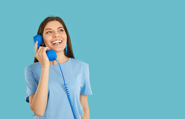 Hotline service. Joyful beautiful young woman talking on retro telephone, isolated on light blue...