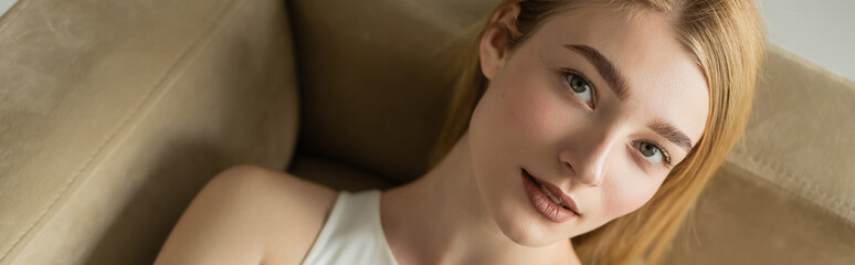 Obraz premium Top view of young woman looking at camera while lying on couch, banner.
