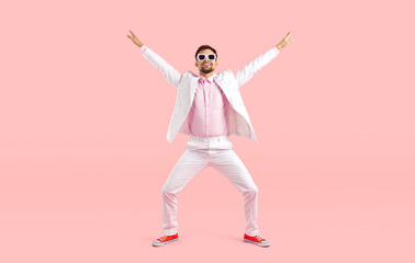 Overjoyed young Caucasian man in suit and converse isolated on pink studio background making moves. Smiling guy in costume have fun dancing and relaxing. Entertainment concept. - obrazy, fototapety, plakaty