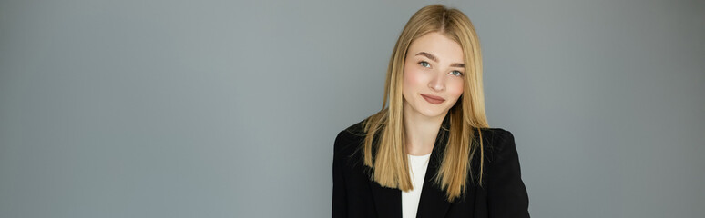 Pretty young woman in black jacket looking at camera near grey wall, banner.