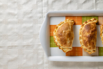 Top view of baked Argentinian empanadas on a platter with copy space.
