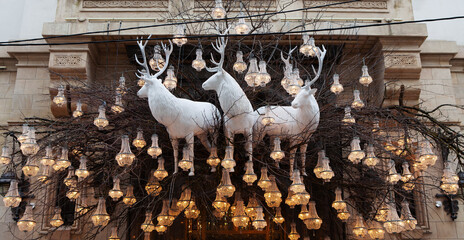 New Year Christmas exteriors. White huge decorative deer in decoration of branches, glowing chandeliers. Christmas decoration on old house background in downtown. Chic luxury designer decorations