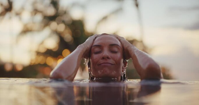 Close up of beautiful woman emerging from the water of luxury resort pool at sunset, relaxing health and wellness spa vacation