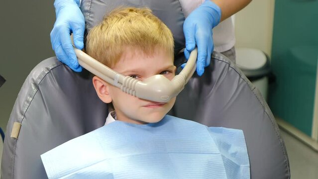 Dentist using nitrous oxide in dental clinic while treating young patients with milk teeth. Relaxation of patient before surgical or dental procedures. Child lying in dental chair with inhalation