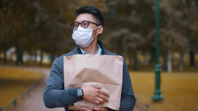 Asian man in mask walk outdoors with paper bag. Realtime