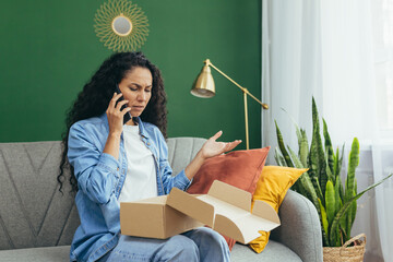 An upset and disappointed buyer in an online store, a woman is not satisfied with the received parcel of goods sits on the sofa and calls the online customer support service to complain.