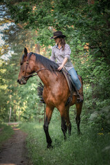 Portrait of a young beautiful girl in a cowboy hat on a horse in the forest.