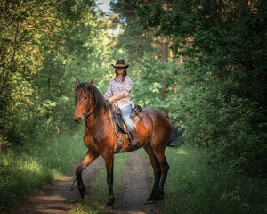 Fototapeta premium Portrait of a young beautiful girl in a cowboy hat on a horse in the forest.