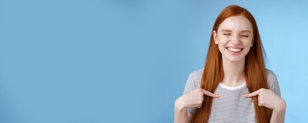 Fototapeta na wymiar Happy cheerful glad young sportswoman redhead nominated smiling surprised laughing joyfully close eyes pointing herself chosen picked winning first prize, standing blue background