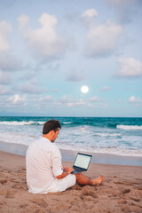 Man with laptop on the beach at sunset 