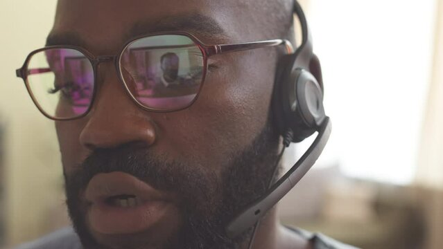Close up of African American man in eyeglasses and headset microphone having video chat with colleague on computer