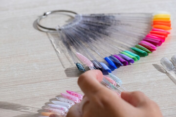 Female hand holds tips with nail polish color shades samples. Fan-shaped plastic tips with metal...
