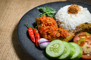 Ayam geprek sambal indonesian food or geprek fried chicken with sambal hot chili sauce served steam rice. Ayam Geprek is a typical Indonesian flour fried chicken dish that is pulverized or crushed