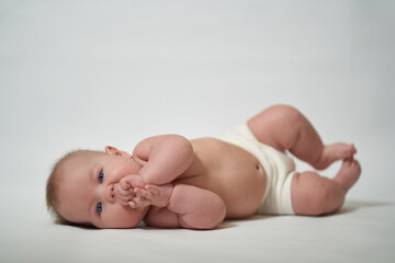 A 2-month-old baby is lying and sucking his fingers on a white background