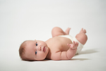 A 2-month-old baby lies on his back and watches and sucks his fingers on a white background
