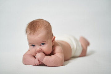 Infant lying on his belly licking his fingers against a white background