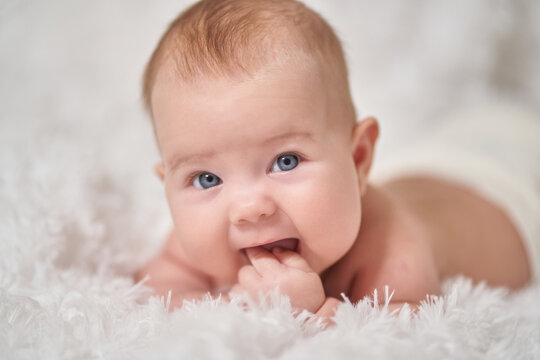 portrait of an infant lying on its stomach on a soft comforter looking at the camera smiling