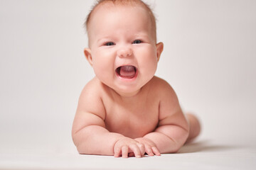 an infant lying on his belly with a cheerful emotion on a white background