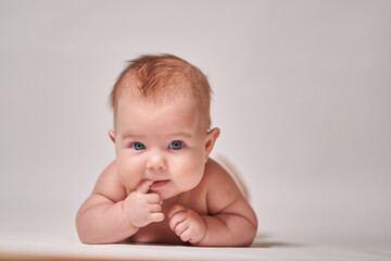 Infant looking into the camera sucking his finger on a white background