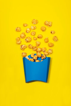 Paper bag with caramel corns scattered on yellow surface