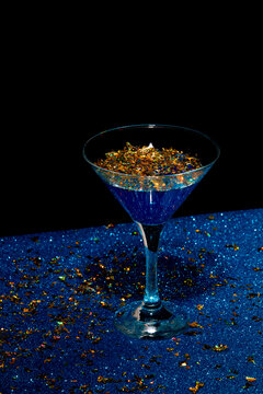 Glass of cocktail with gold foil flakes on table