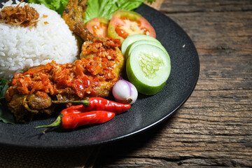 Ayam geprek sambal indonesian food or geprek fried chicken with sambal hot chili sauce served steam rice on black plate