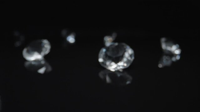 Slow push in on round classic diamond in dark black surface and background. Various diamond stones set on reflective floor as camera moves close stopping on one diamond