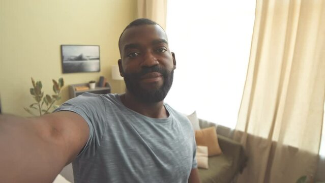 Handheld shot of African American man video chatting with friend at home or recording video blog of him talking at camera