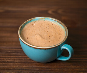 Big blue cup with cappuccino on wooden background