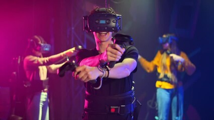 A joyful, interested boy is playing on VR treadmill with helmet, controllers and backpack. Other people playing nearby. Slow motion