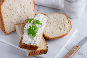 Home made bread on a wooden cutting board with curd cheese and parsley. Decorated with green herbs