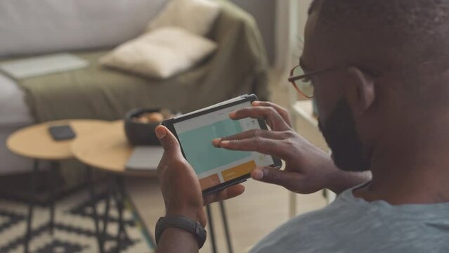 Black man using digital tablet while working from home, zooming web site page and reading information
