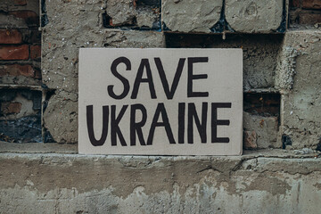 Ukrainian protest against war with banner placard  with inscription message text Save Ukraine, ruined city background. Crisis, peace, Russian aggression invasion concept. anti-war demonstration.