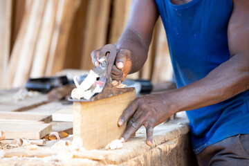 Portrait of an African carpenter planing a board in a carpentry workshop on a table. - obrazy, fototapety, plakaty
