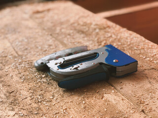 Metallic blue stapler for stapling lies in sawdust on a wooden rafter beam on the roof in focus...