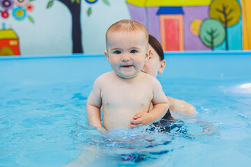 Fototapeta na wymiar A swimming teacher teaches a little boy to swim in the pool. Children's first swimming lessons. Development for babies