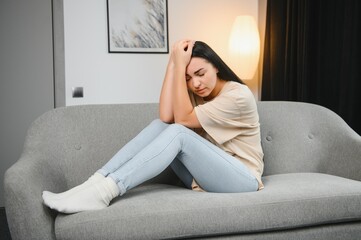 Depressed sad attractive woman crying on sofa couch at home feeling lonely tired and worried suffering depression in mental health, loneliness and isolation concept. Psychology, solitude and people.