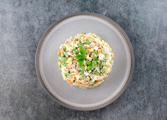 Russian Olivier salad of vegetables, sausage and mayonnaise on a gray background. Top view, copy space.